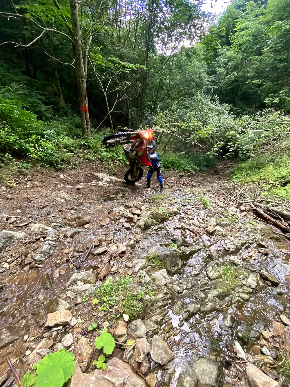 Rider lifting his KTM over boulders in a rocky mountain stream