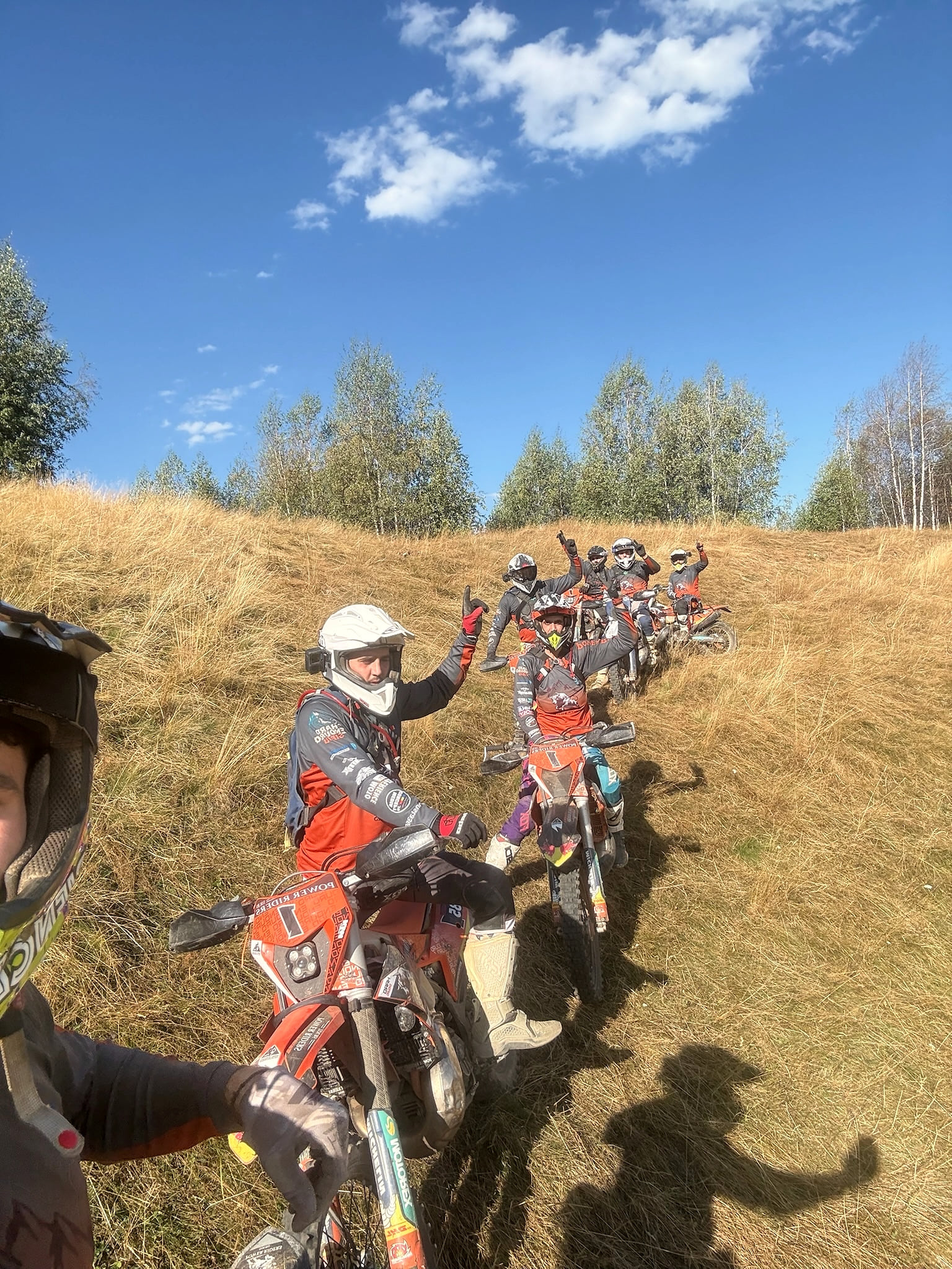 A long line of enduro bikes on a dry hillside, a rider in front waving