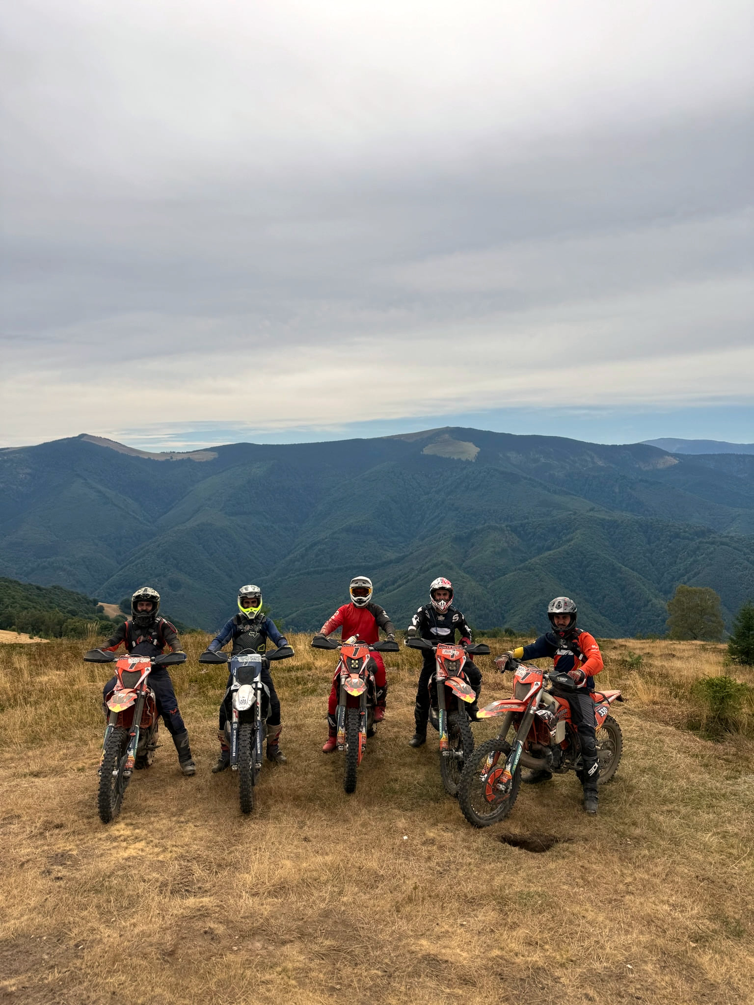 Five riders on their enduro bikes on a dusty plateau, mountains behind