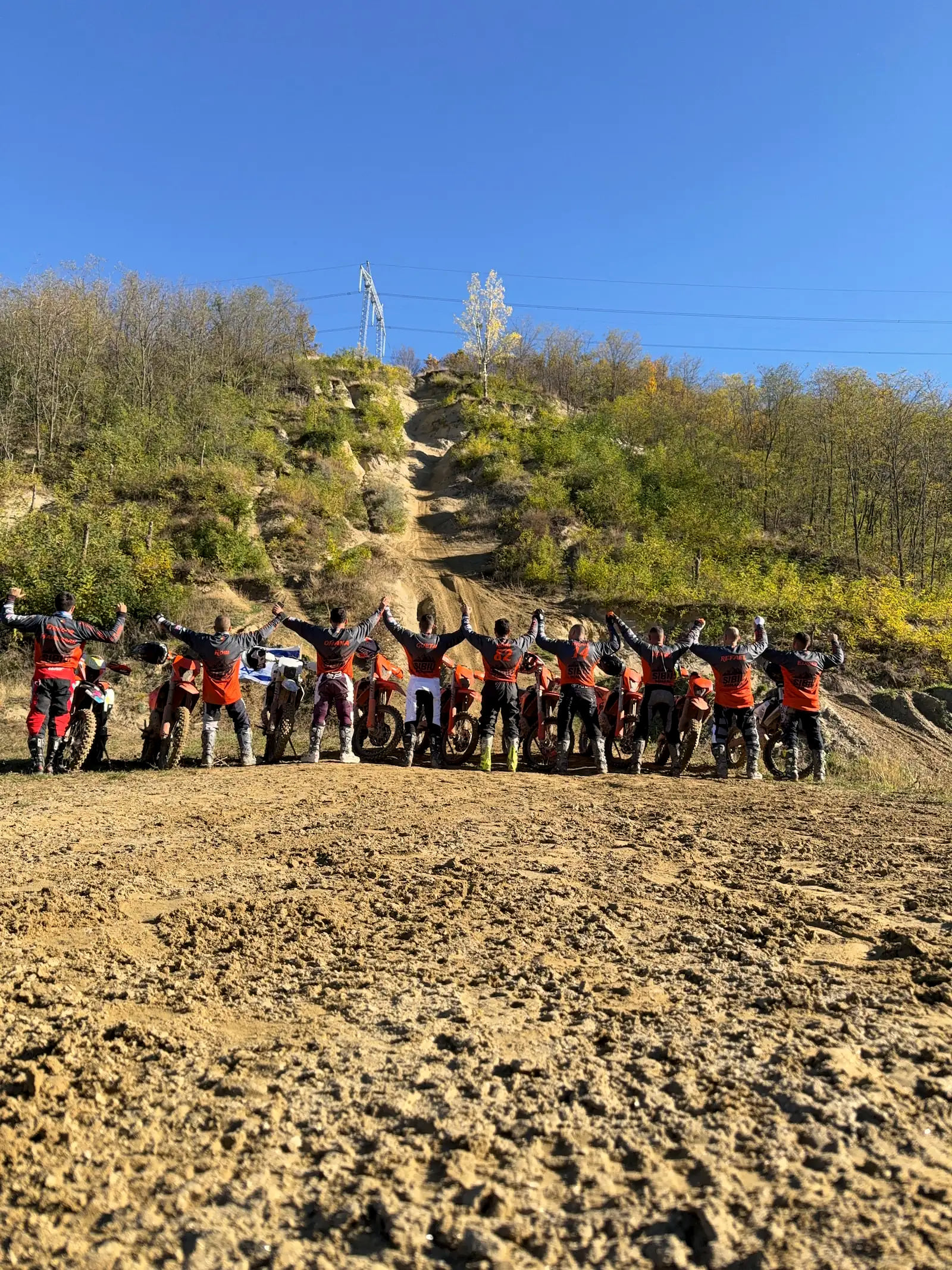 Group of nine riders with their KTM bikes at the foot of a sand hill climb in Romania