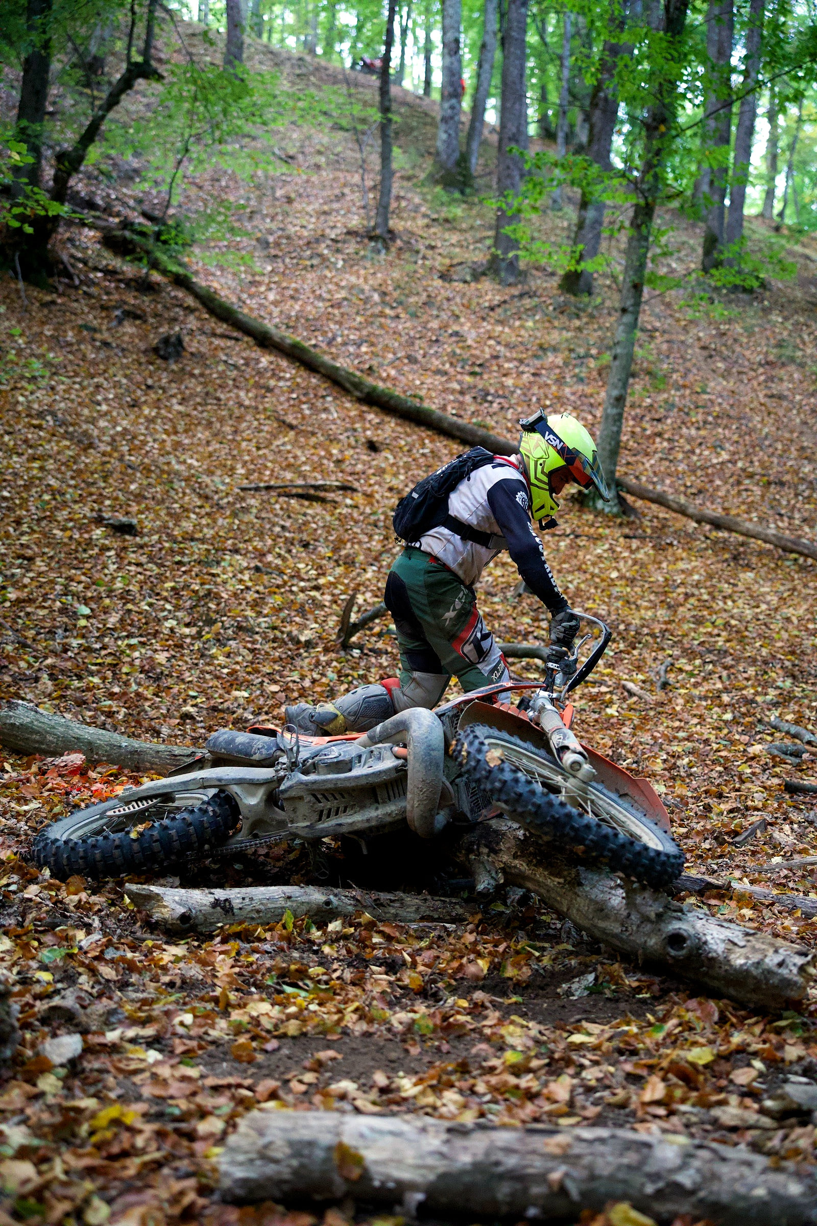 Rider lifting his bike after dropping it over a fallen log on a wet slope