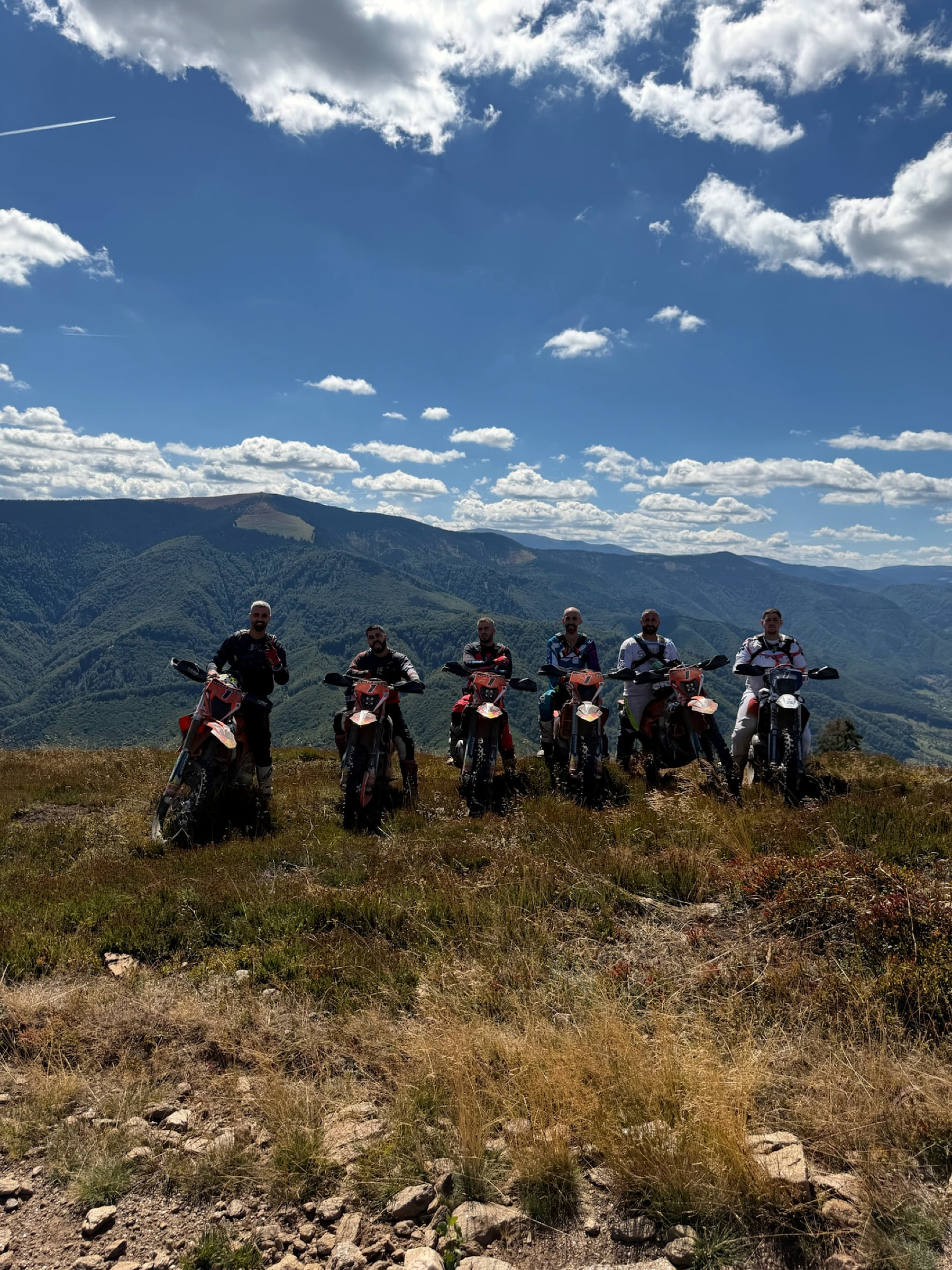 Group of six riders on their bikes along a grassy ridge in the mountains