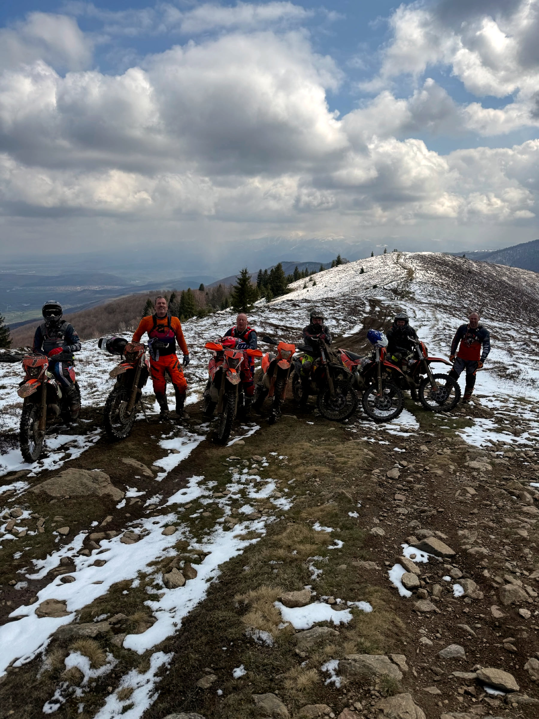 Line of enduro riders on a snowy ridge track under broken cloud in the mountains