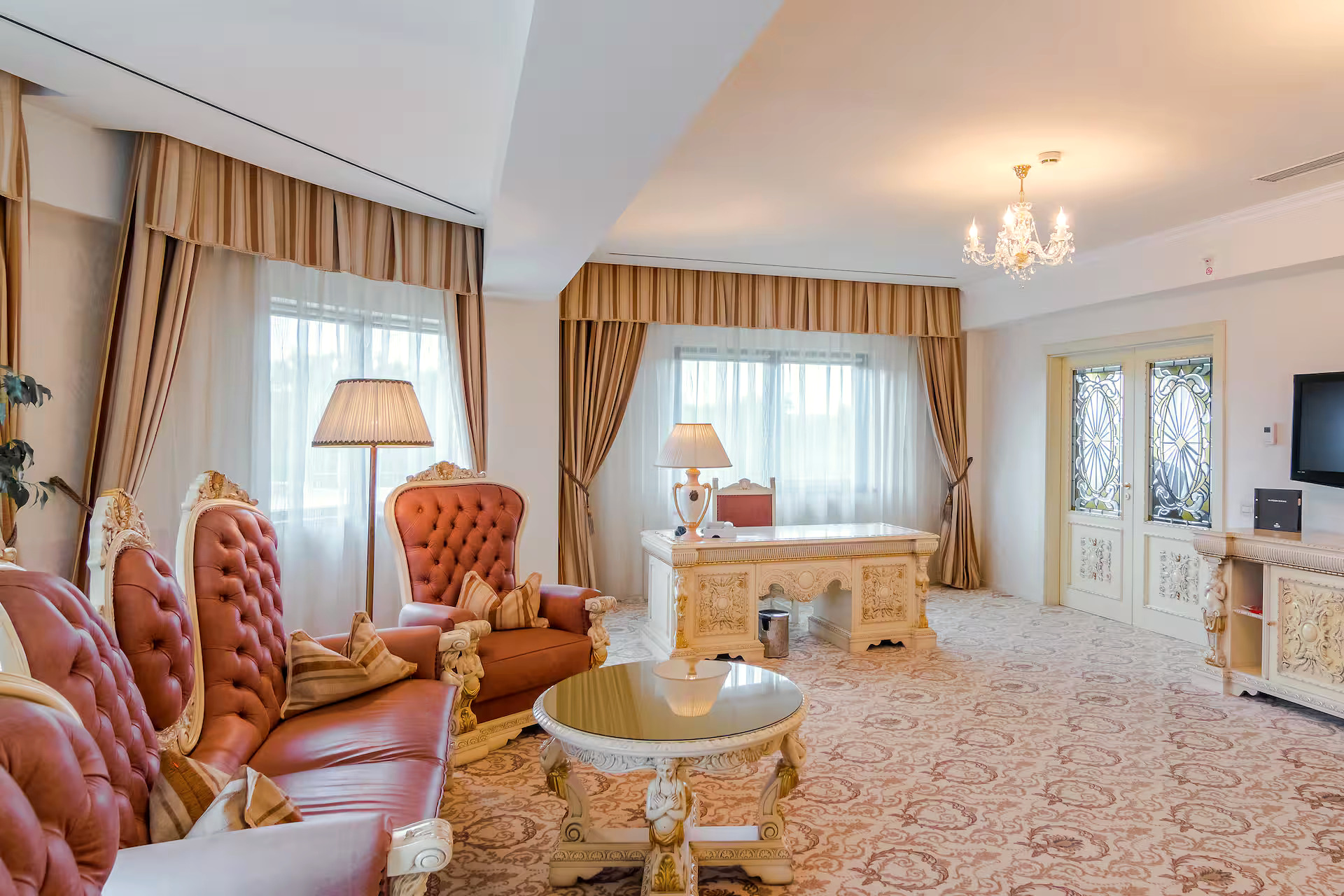 A suite at the Hilton Sibiu: a sitting room with tufted leather armchairs, a carved desk and a chandelier.