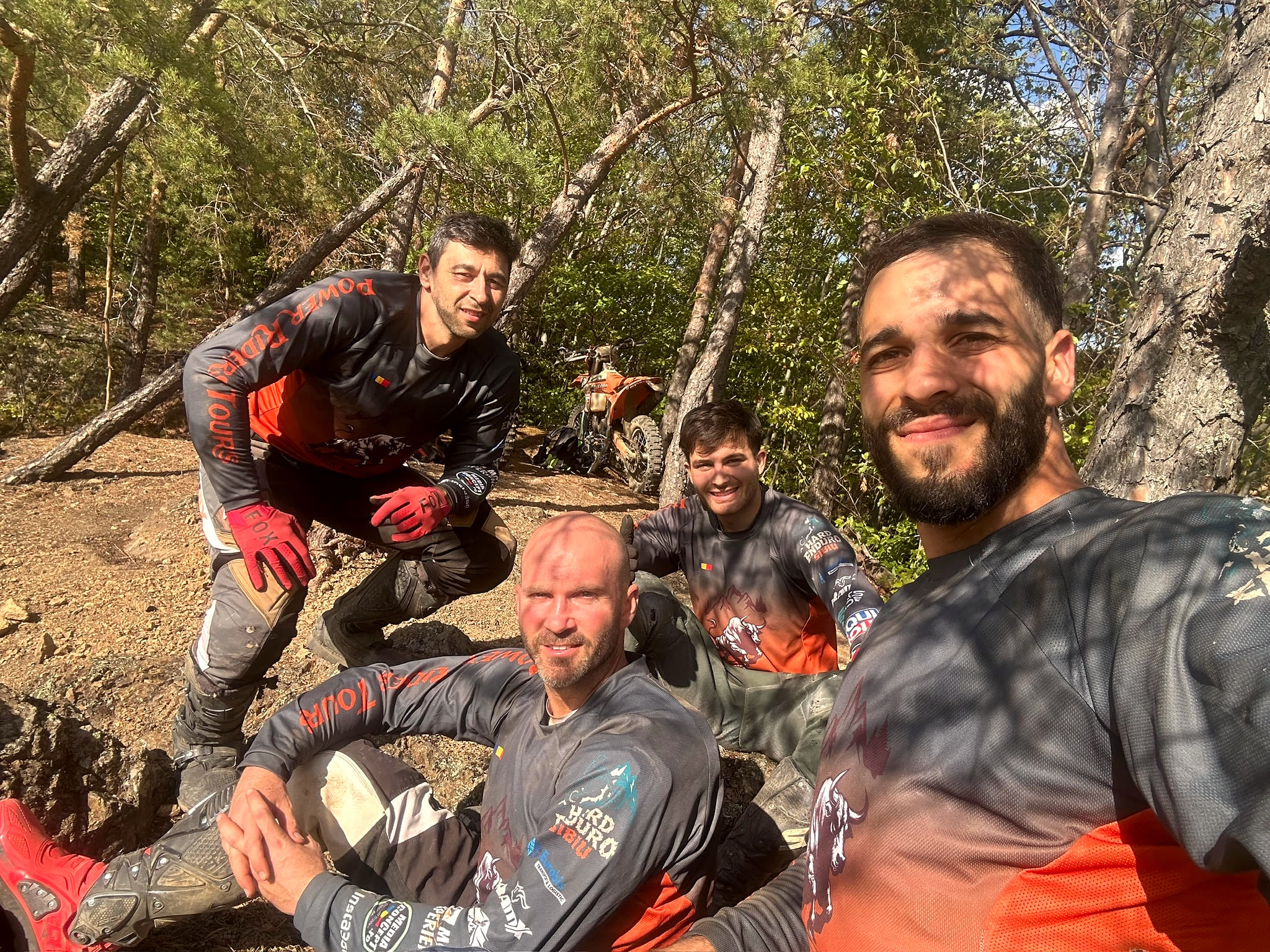 Four riders in their gear take a selfie on the forest floor during a break