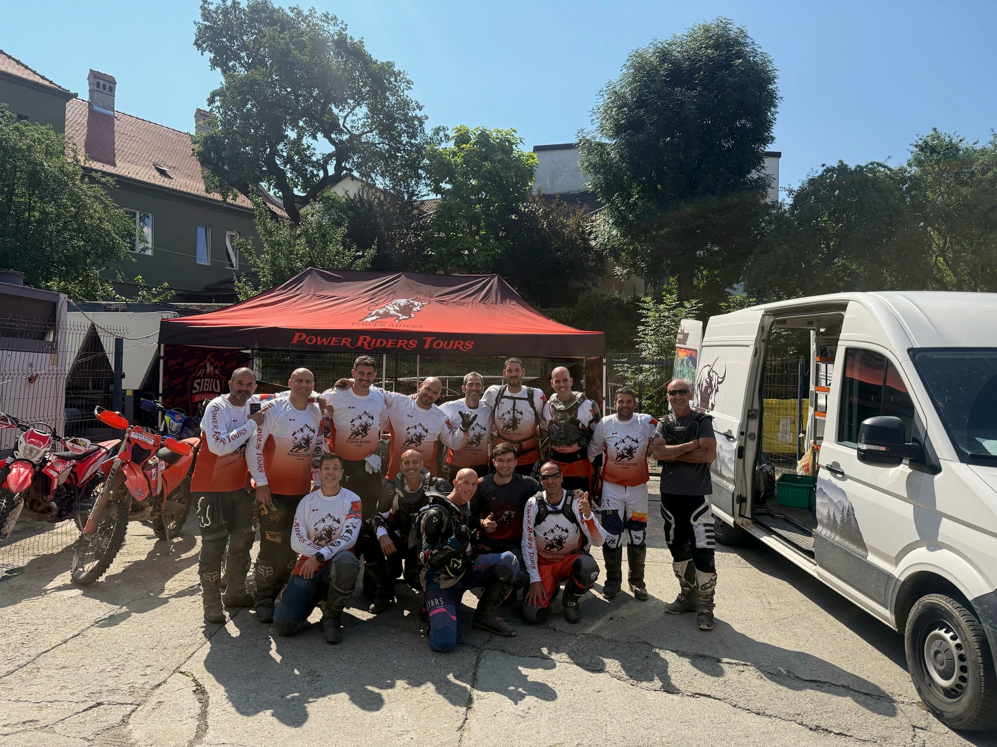 A large group of riders in their gear in front of the Power Riders Tours tent and support van at the hotel