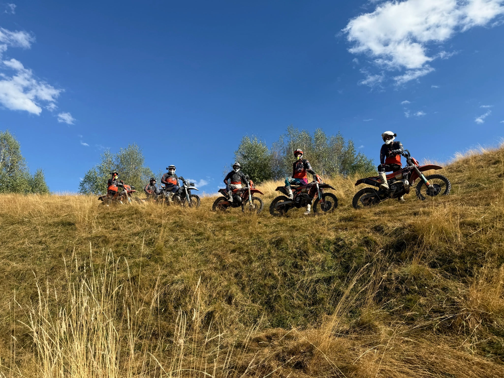 A group of riders on their bikes spread across a dry mountain meadow under a blue sky