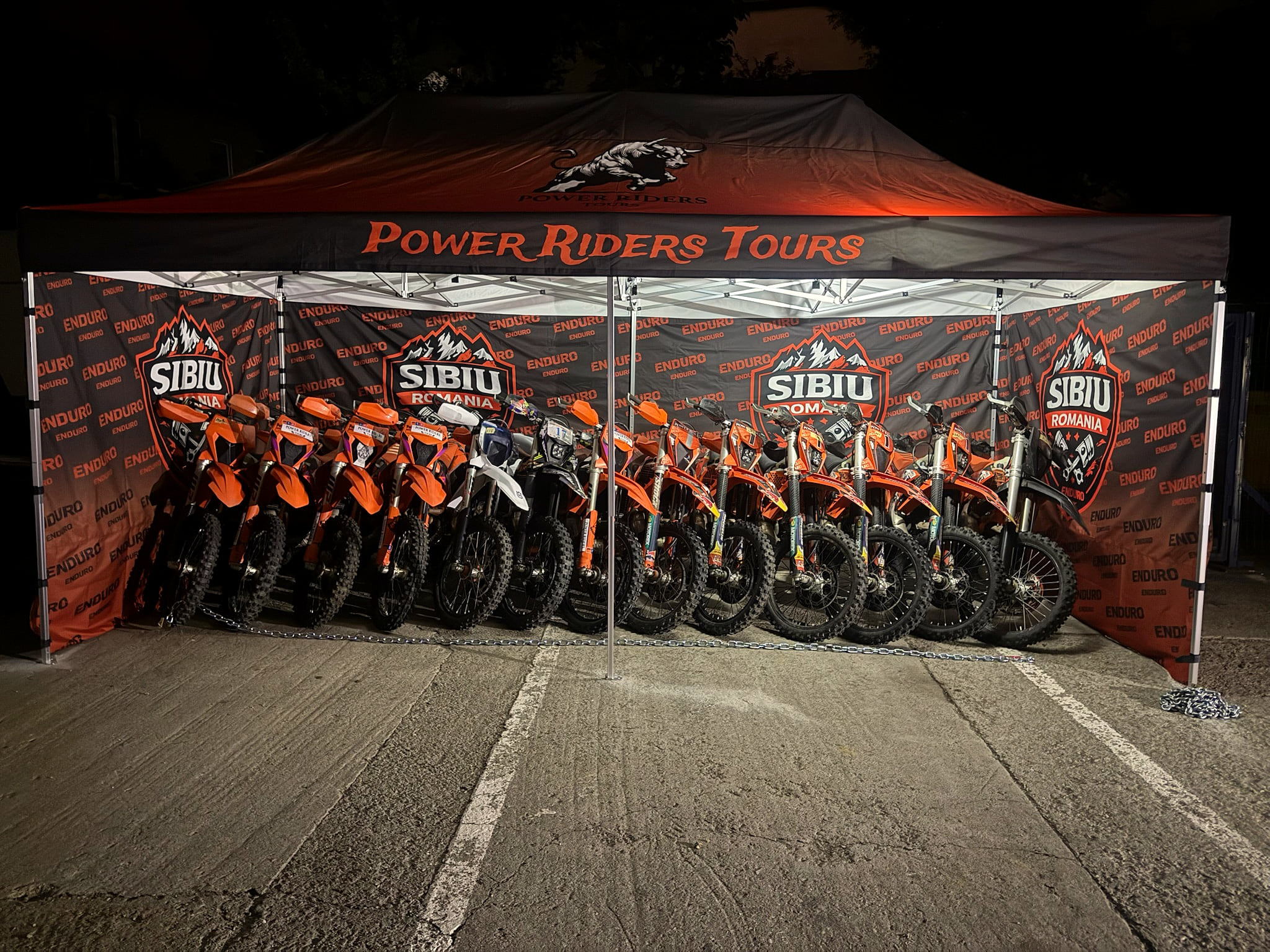 Orange KTM-Enduro-Bikes aufgereiht unter dem Zelt von Power Riders Tours, an den Wänden Sibiu-Banner.