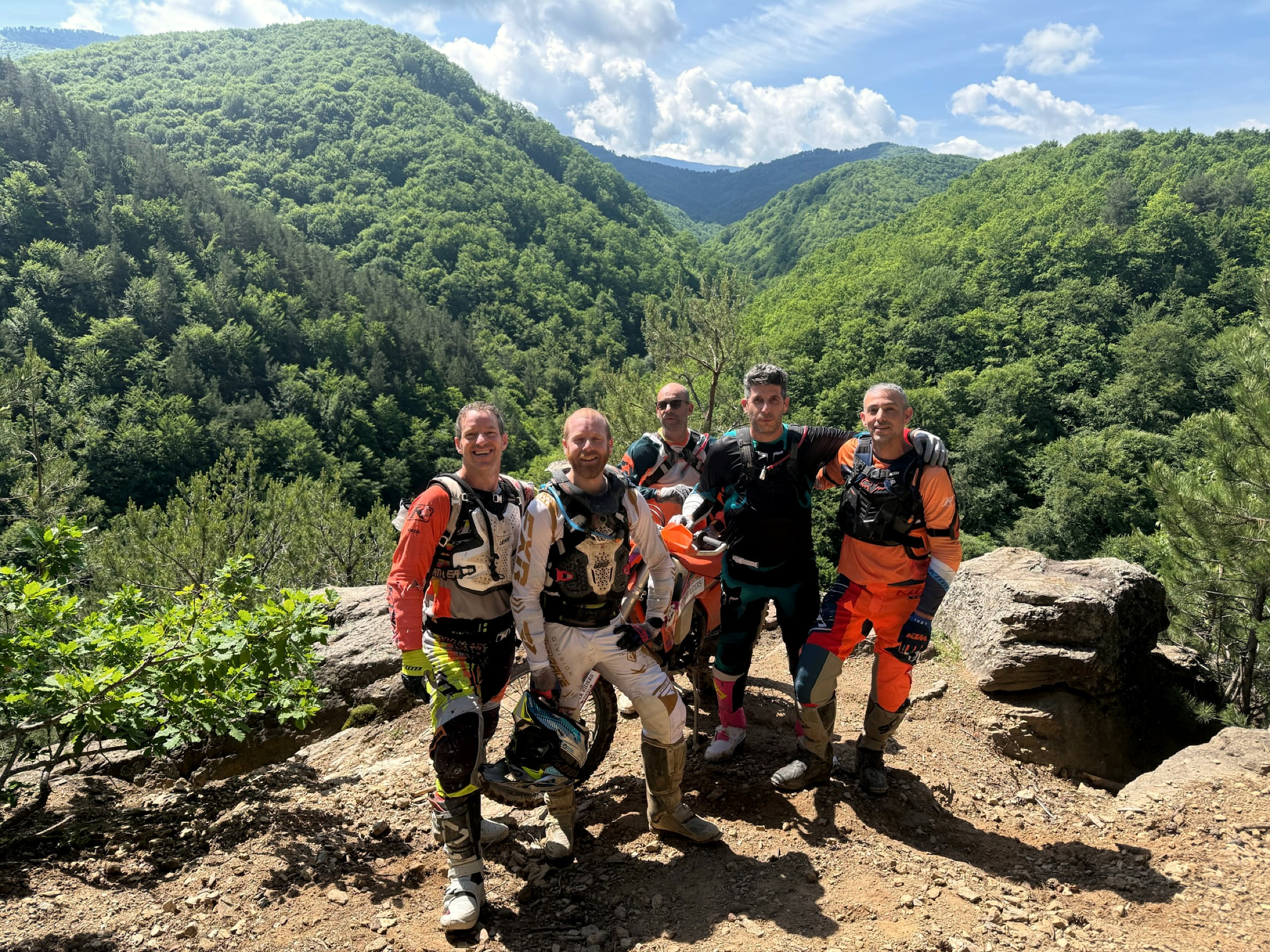 Group of five riders on a rock outcrop above a forested valley in the mountains