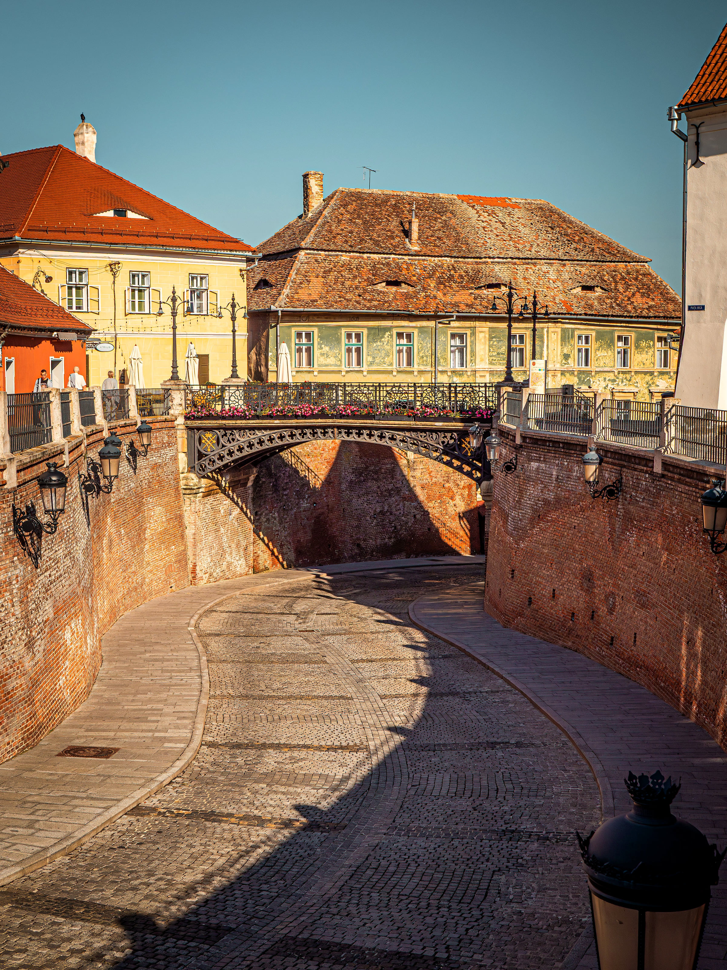 The cast-iron Bridge of Lies over a cobbled lane in Sibiu's old town, old houses with red roofs above it.