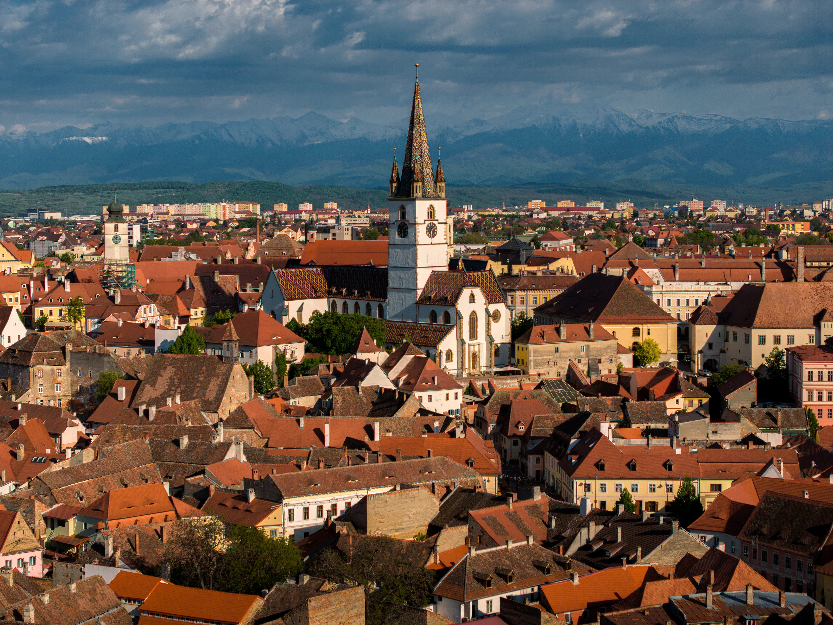 Rote Dächer der Altstadt von Sibiu rund um den Turm der Stadtpfarrkirche, am Horizont schneebedeckte Berge.