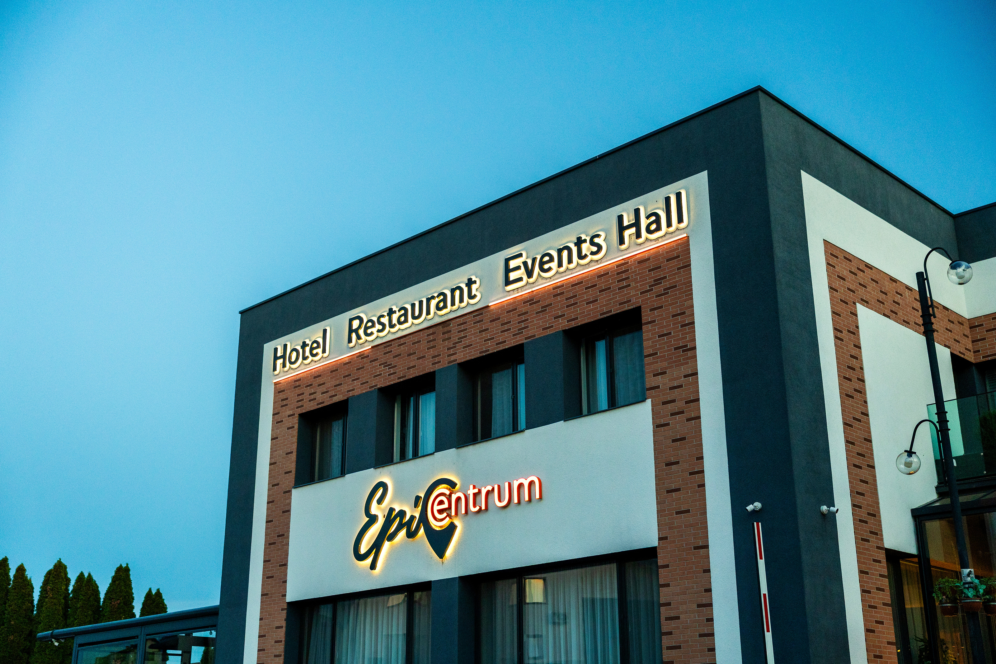 The Epic Centrum Hotel at dusk: its lit name and a Hotel, Restaurant, Events Hall sign on a brick and white front.