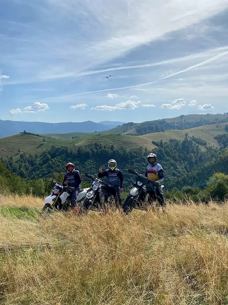 Three riders on their enduro bikes in tall summer grass on a meadow in the mountains